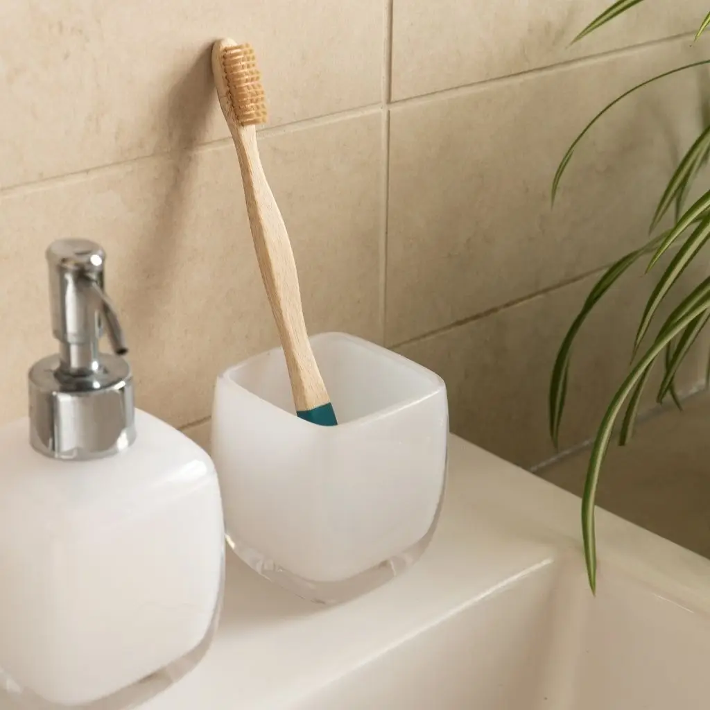 A bamboo toothbrush rests in a white holder next to a soap dispenser, integrating seamlessly into a minimalist and eco-conscious bathroom decor.